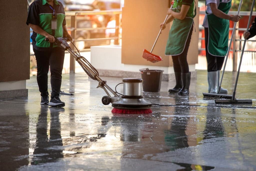Professional cleaning crew using an industrial floor scrubber and squeegees on a commercial lobby floor