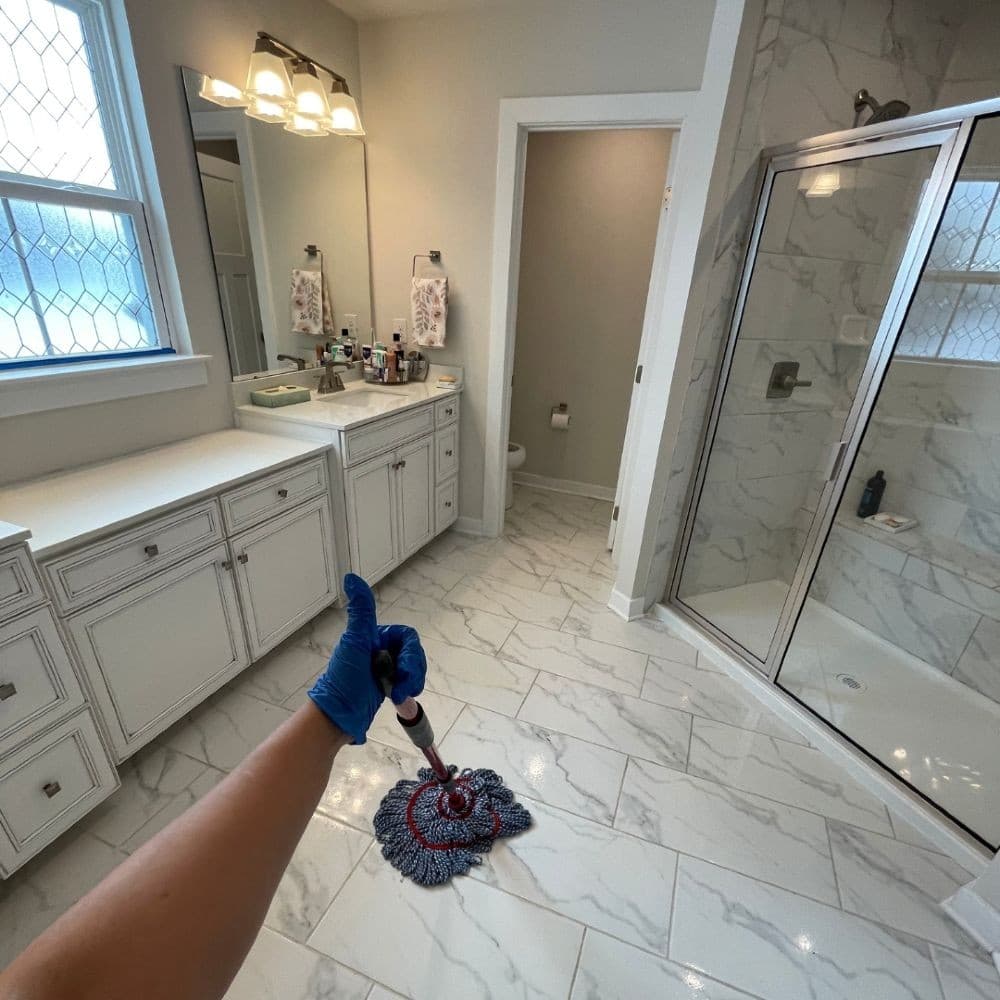 Cleaner giving a thumbs-up in a freshly mopped new-build bathroom with marble tiles and walk-in shower
